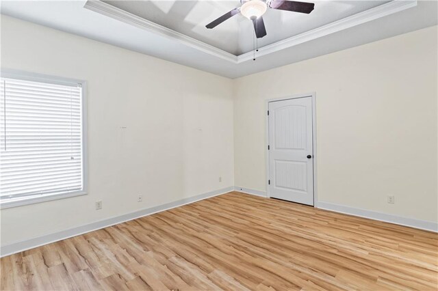 spare room with light wood-type flooring, a tray ceiling, crown molding, and a ceiling fan