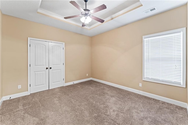 unfurnished bedroom with a tray ceiling, visible vents, ornamental molding, carpet flooring, and baseboards