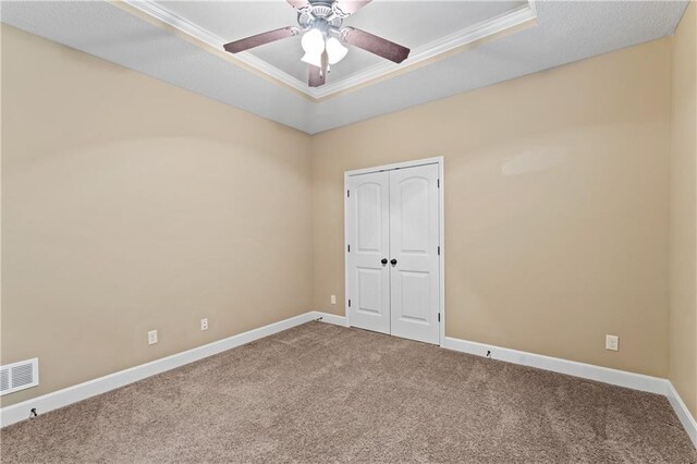 carpeted spare room with a ceiling fan, visible vents, baseboards, a tray ceiling, and crown molding