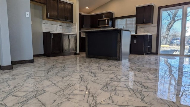 kitchen featuring marble finish floor, light countertops, stainless steel microwave, and vaulted ceiling