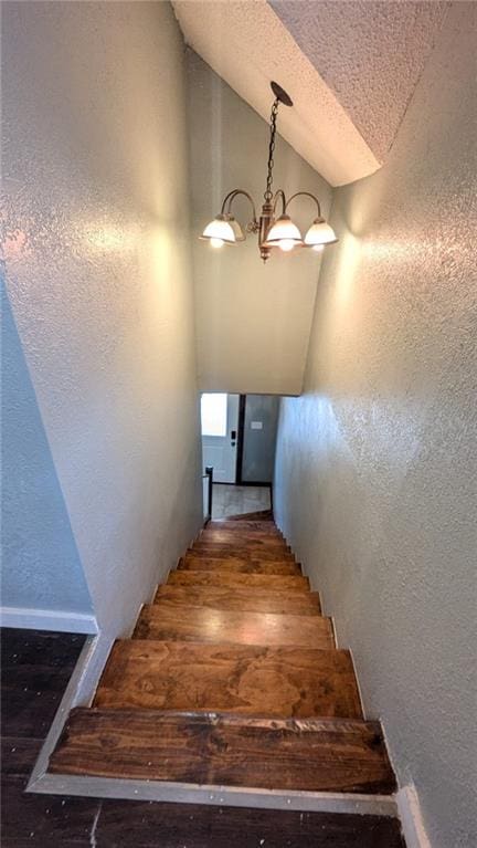 stairs with lofted ceiling, a textured wall, a textured ceiling, a notable chandelier, and wood finished floors