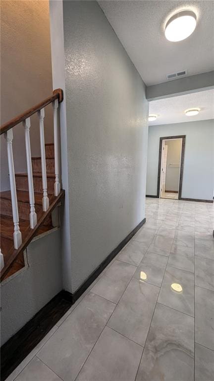 hallway featuring a textured ceiling, stairway, visible vents, and baseboards