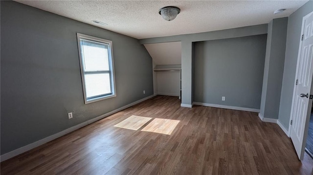 additional living space featuring a textured ceiling, wood finished floors, and baseboards