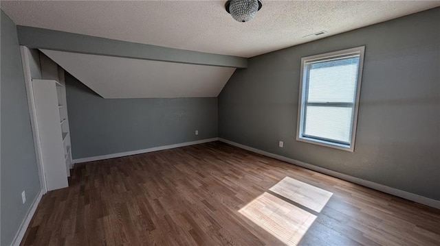 bonus room featuring vaulted ceiling with beams, visible vents, a textured ceiling, and wood finished floors