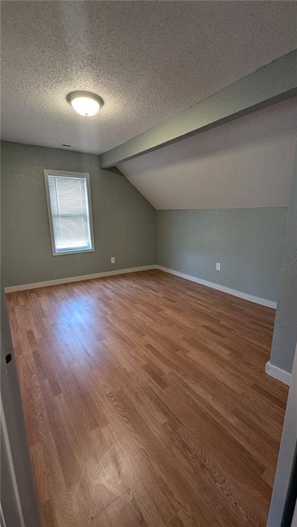 bonus room with lofted ceiling, a textured ceiling, wood finished floors, and baseboards