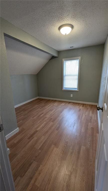 additional living space with vaulted ceiling, a textured ceiling, baseboards, and wood finished floors