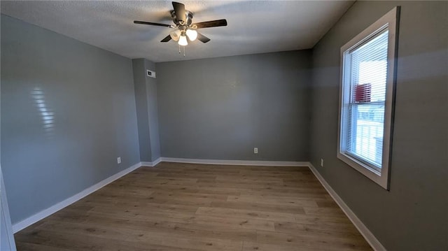 unfurnished room featuring a wealth of natural light, ceiling fan, baseboards, and wood finished floors