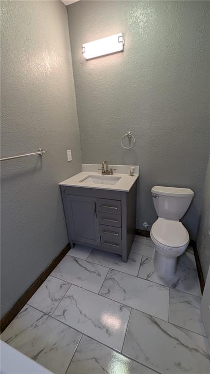 bathroom featuring a textured wall, toilet, vanity, baseboards, and marble finish floor