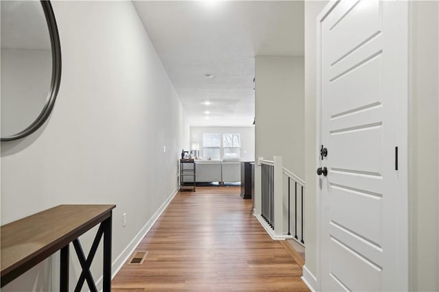 corridor featuring visible vents, baseboards, and wood finished floors