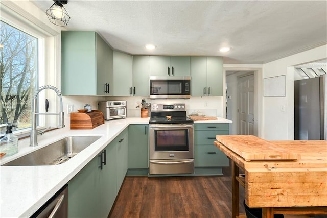 kitchen with a sink, stainless steel appliances, green cabinetry, and light countertops