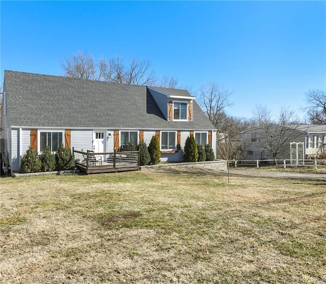 view of front facade with a wooden deck, fence, roof with shingles, and a front yard