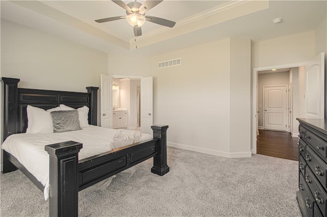 carpeted bedroom with baseboards, visible vents, a raised ceiling, ensuite bath, and ceiling fan