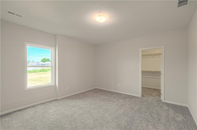 unfurnished bedroom featuring a walk in closet, carpet flooring, visible vents, and baseboards