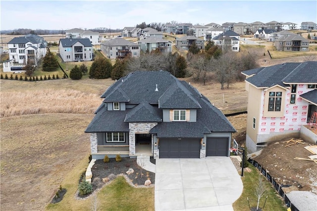 view of front facade featuring stone siding, a shingled roof, a residential view, and concrete driveway