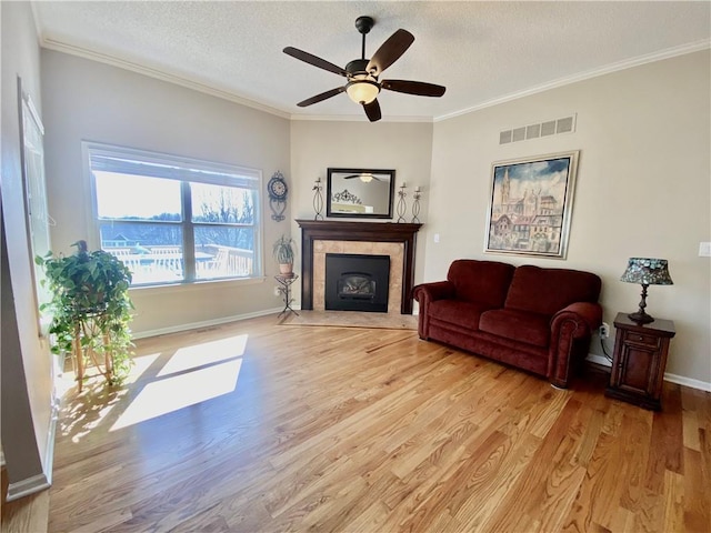 living area featuring visible vents, a fireplace with flush hearth, a textured ceiling, crown molding, and light wood-type flooring