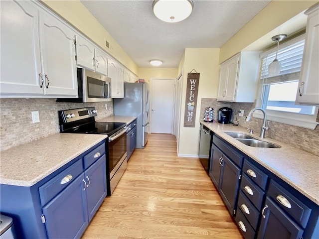 kitchen with light wood finished floors, appliances with stainless steel finishes, white cabinetry, blue cabinets, and a sink