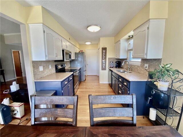 kitchen featuring a sink, stainless steel appliances, light countertops, blue cabinets, and light wood-type flooring