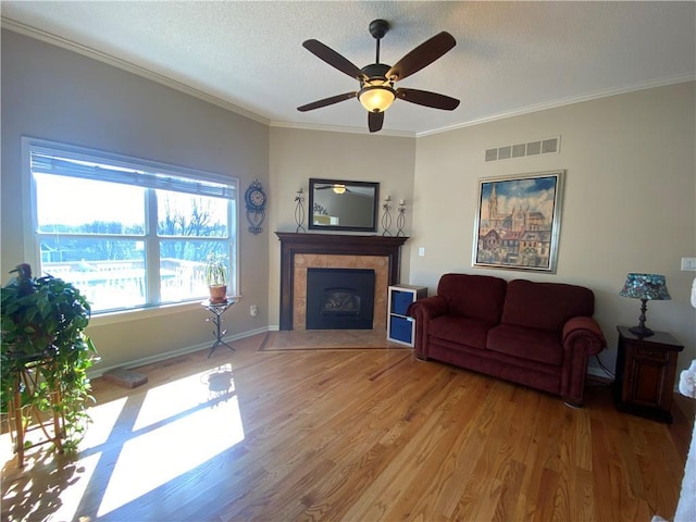 living area featuring visible vents, ornamental molding, a textured ceiling, a fireplace, and light wood finished floors