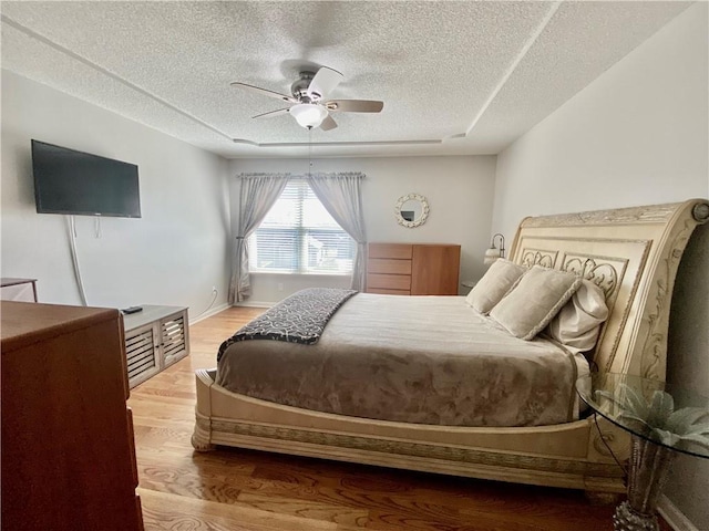 bedroom with baseboards, a textured ceiling, ceiling fan, and wood finished floors