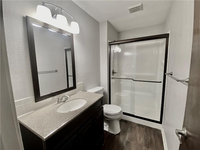 bathroom featuring visible vents, toilet, wood finished floors, a shower stall, and vanity