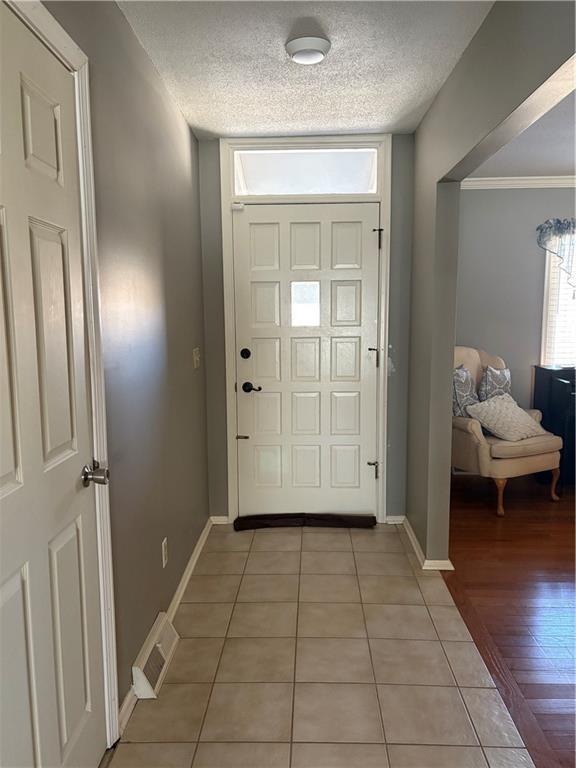 entrance foyer featuring a textured ceiling, light tile patterned floors, visible vents, baseboards, and ornamental molding