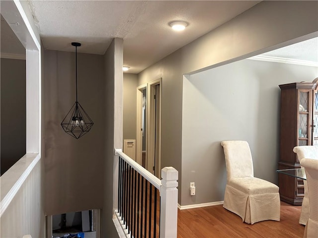 corridor featuring a textured ceiling, baseboards, wood finished floors, and an upstairs landing