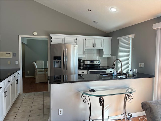 kitchen featuring dark countertops, lofted ceiling, appliances with stainless steel finishes, white cabinets, and a sink