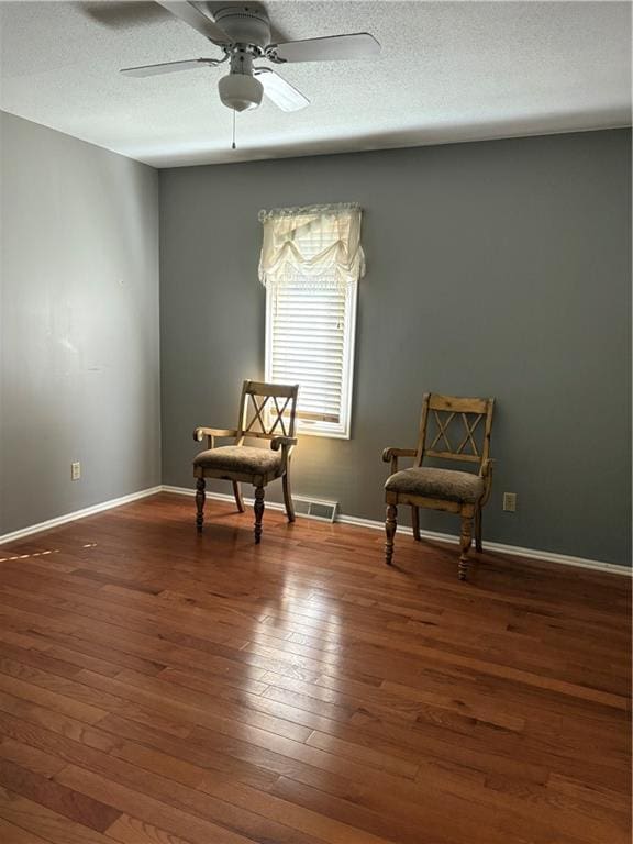 living area featuring hardwood / wood-style flooring, ceiling fan, baseboards, and a textured ceiling