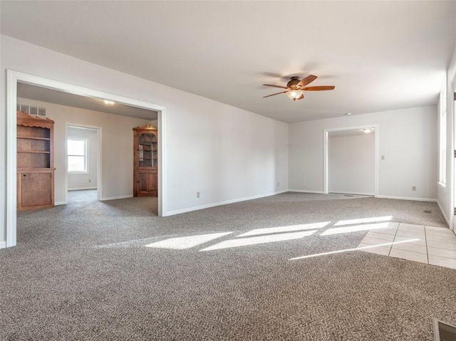 carpeted empty room featuring a ceiling fan, tile patterned flooring, visible vents, and baseboards