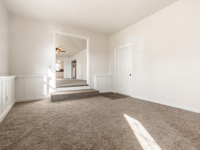 empty room featuring a wainscoted wall, carpet, stairs, and a decorative wall