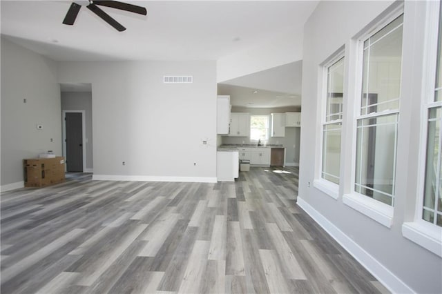 unfurnished living room featuring a sink, a ceiling fan, wood finished floors, visible vents, and baseboards