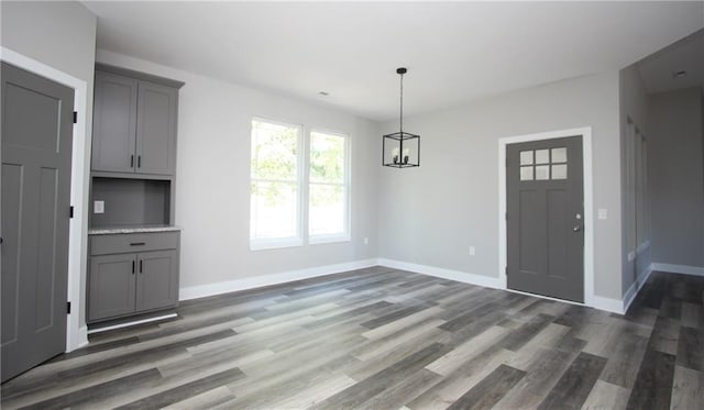 unfurnished dining area featuring a chandelier, baseboards, and wood finished floors