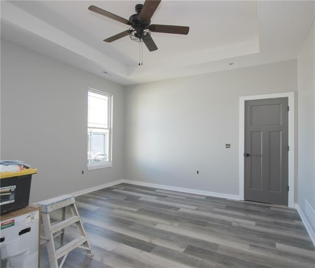 spare room with ceiling fan, baseboards, a raised ceiling, and wood finished floors