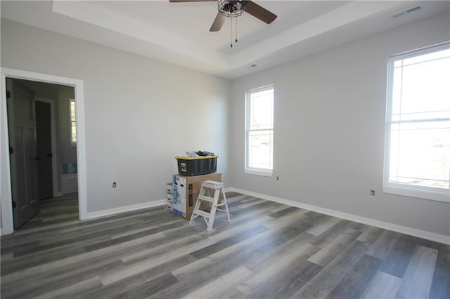 spare room featuring a tray ceiling, wood finished floors, visible vents, and baseboards