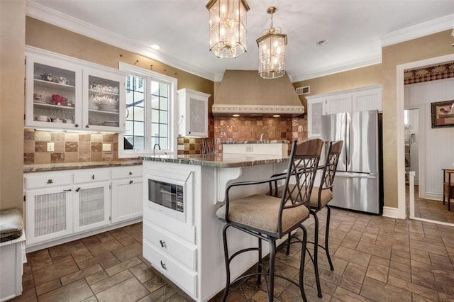 kitchen featuring white cabinets, white microwave, freestanding refrigerator, and stone tile floors