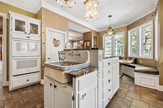 kitchen with double oven, a sink, breakfast area, stone tile flooring, and crown molding