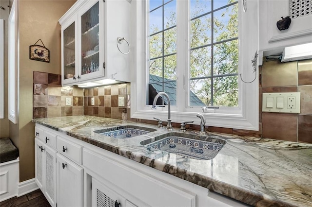 kitchen with a wealth of natural light, tasteful backsplash, stone counters, and glass insert cabinets