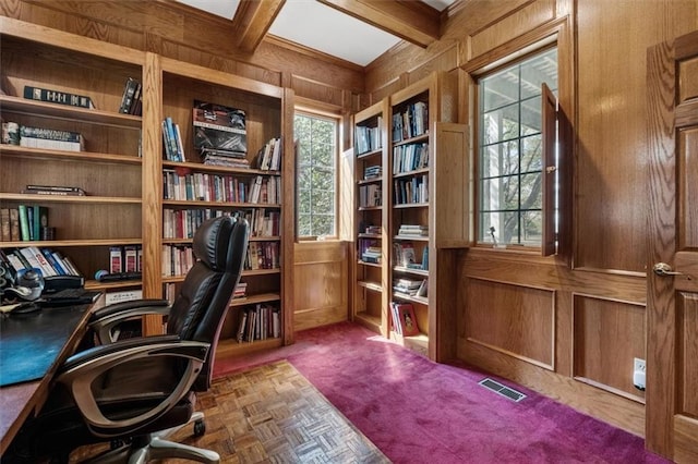 carpeted office space with coffered ceiling, beam ceiling, visible vents, and wooden walls