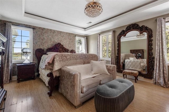 bedroom featuring visible vents, a tray ceiling, light wood-style flooring, and crown molding