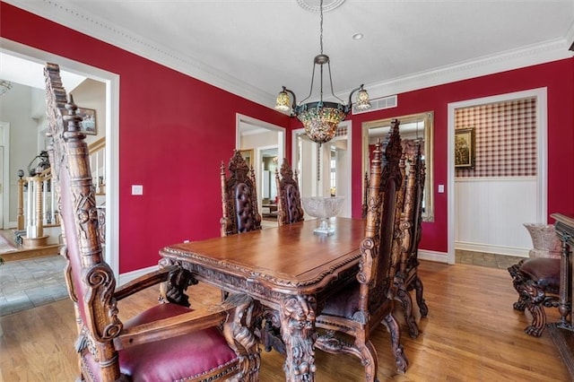 dining area with a wainscoted wall, wood finished floors, an inviting chandelier, stairs, and crown molding