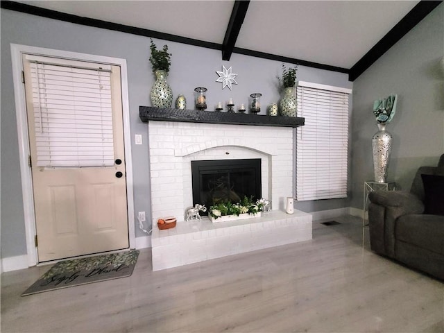 living room featuring a brick fireplace, visible vents, vaulted ceiling with beams, and baseboards