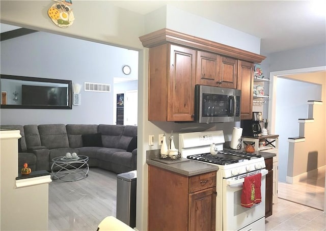 kitchen featuring white range with gas stovetop, visible vents, dark countertops, stainless steel microwave, and brown cabinets