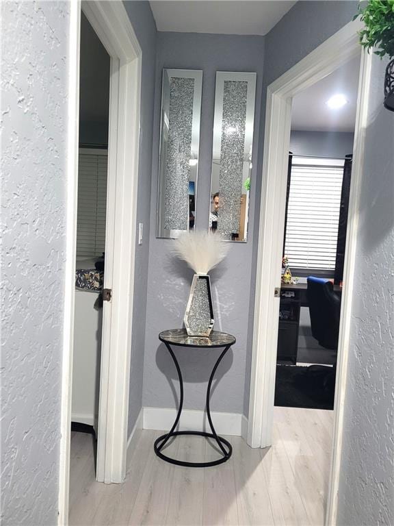 hallway with a textured wall, baseboards, and wood finished floors