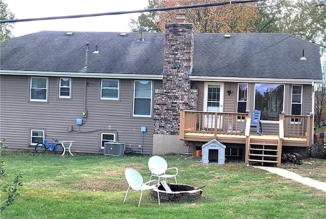 rear view of property featuring an outdoor fire pit, a chimney, a lawn, and a deck