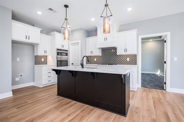 kitchen featuring visible vents, a breakfast bar area, hanging light fixtures, light wood-type flooring, and white cabinetry