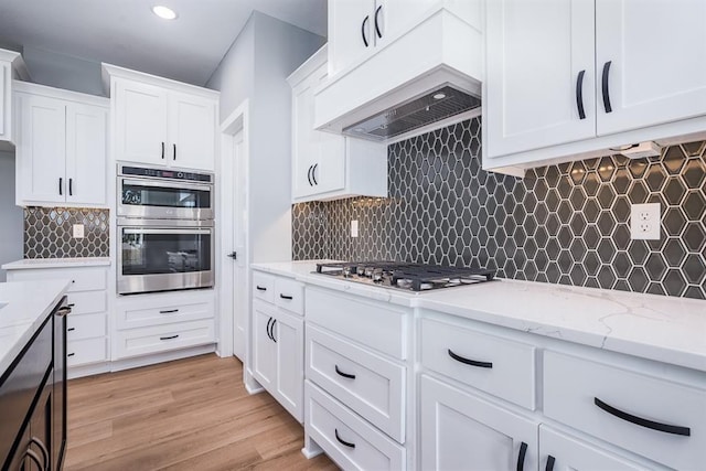 kitchen featuring premium range hood, appliances with stainless steel finishes, backsplash, and light wood-style floors