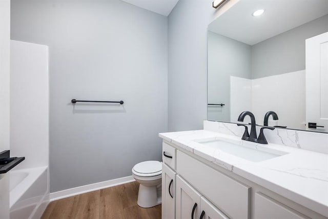 bathroom with toilet, vanity, wood finished floors, baseboards, and a bath