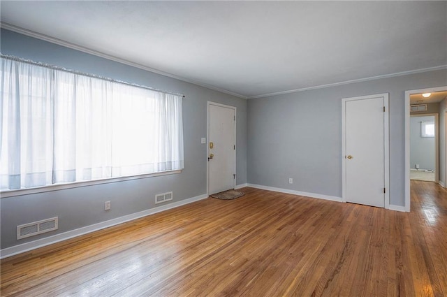 empty room featuring ornamental molding, wood finished floors, visible vents, and baseboards