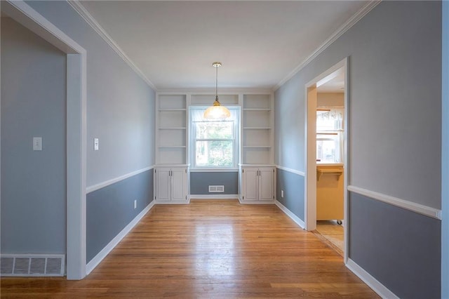 unfurnished dining area featuring baseboards, wood finished floors, visible vents, and crown molding