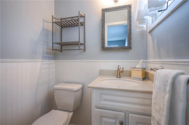 half bathroom featuring wainscoting, vanity, and toilet